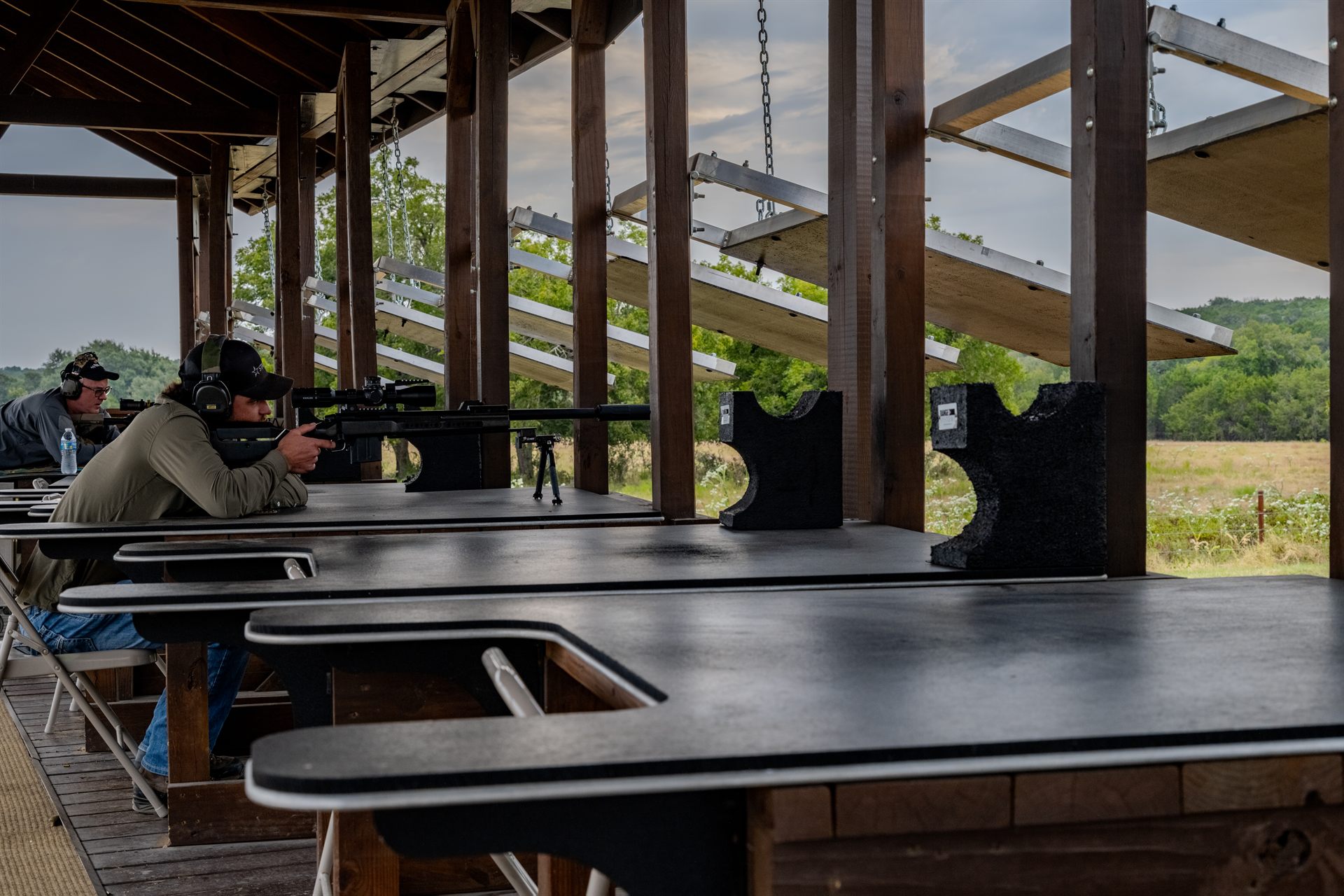 A shooter on a bipod-mounted precision rifle at a covered bench on the Long Range course at Staccato Ranch Texas.