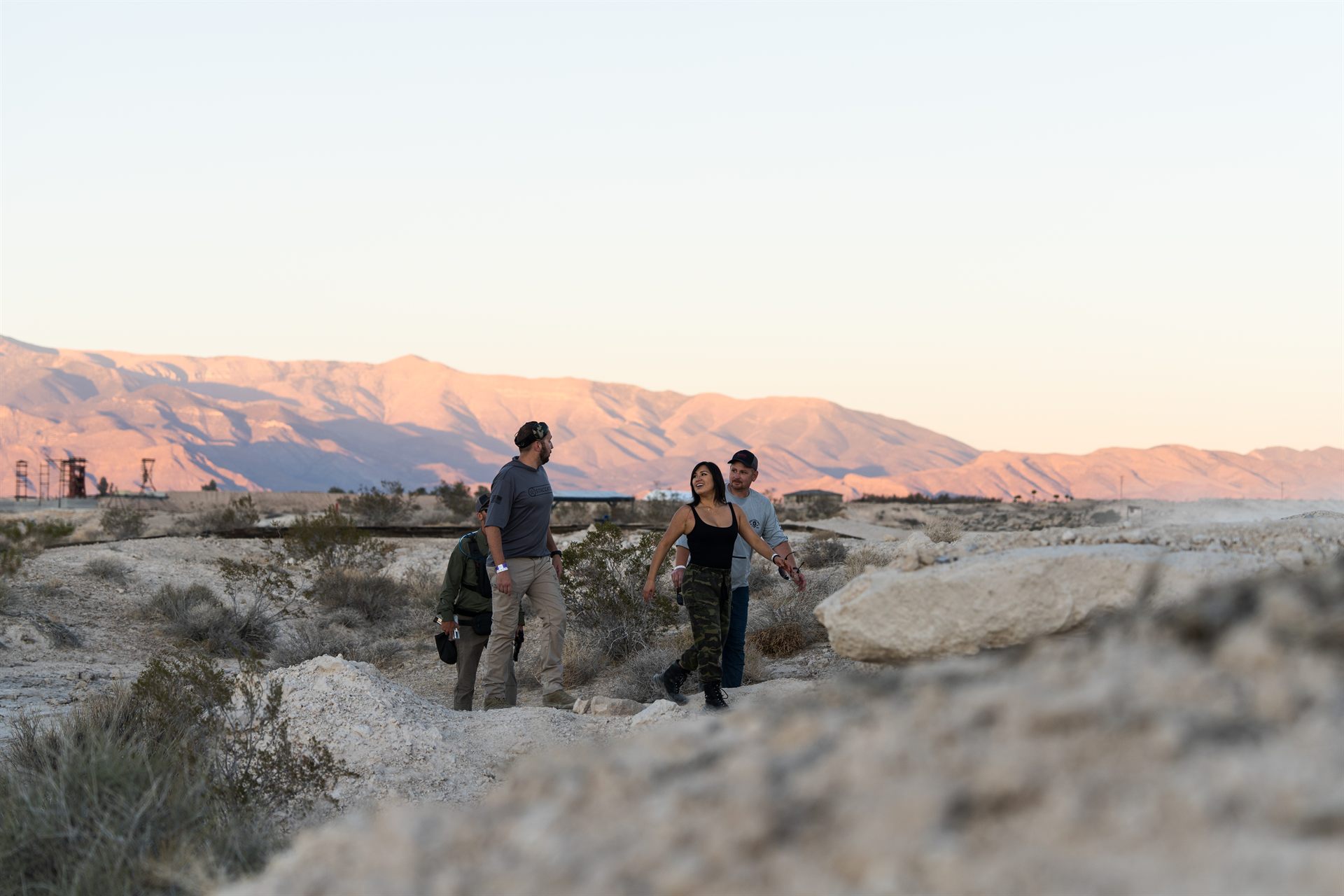 Three visitors walking the Nevada high desert at sunset, mountains beyond